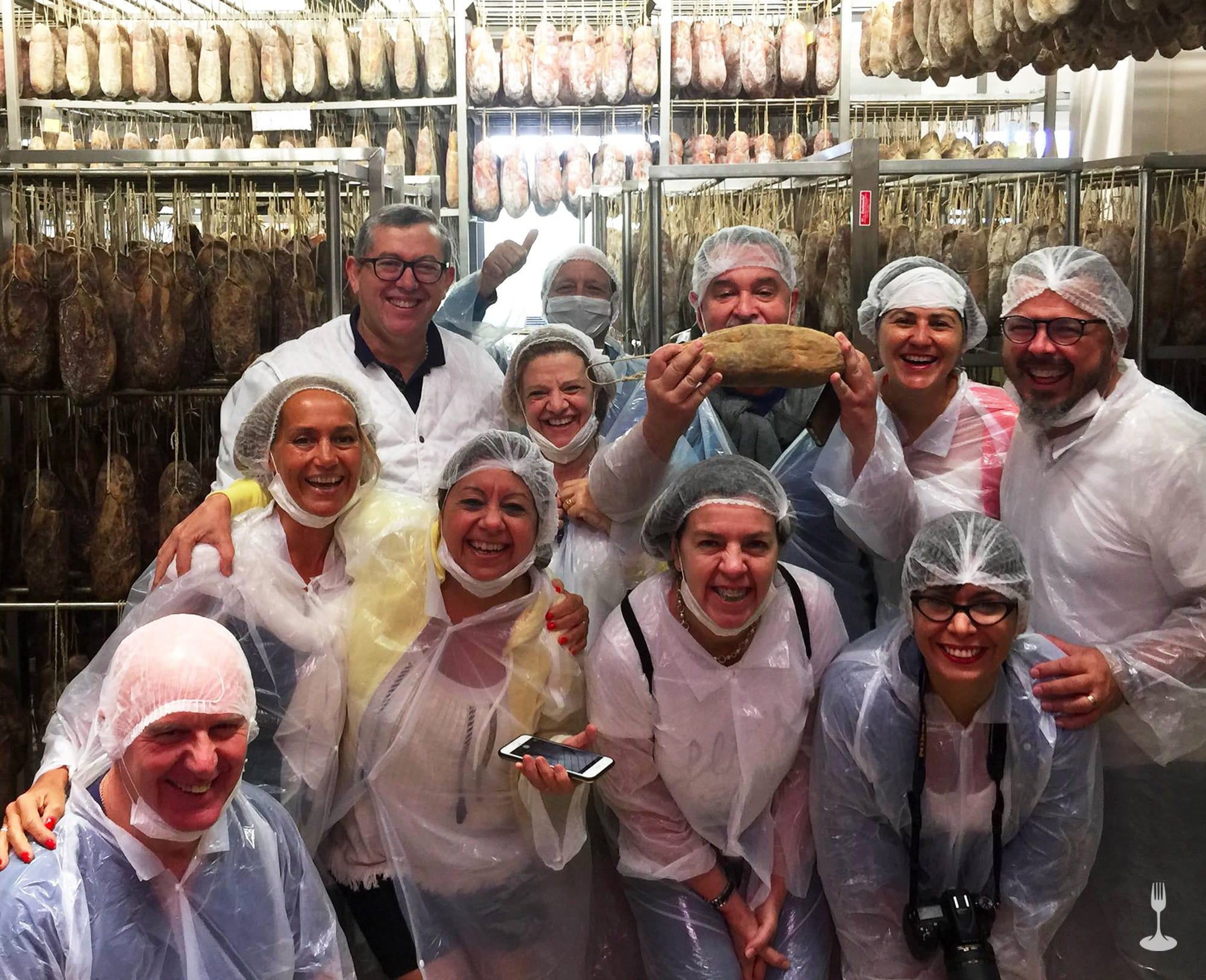 Ospiti soddisfatti fanno la foto di gruppo con alle spalle numerosi salumi appesi Ospiti soddisfatti fanno la foto di gruppo con alle spalle numerosi salumi appesi