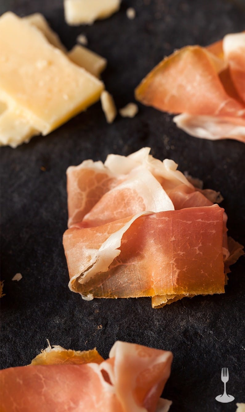 Assaggini di prosciutto e formaggi serviti su tagliere di colore nero Assaggini di prosciutto e formaggi serviti su tagliere di colore nero