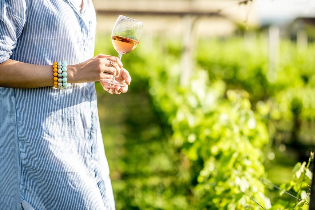 Profilo di donna con calice di vino rosato in mano mentre passeggia in un vigneto.