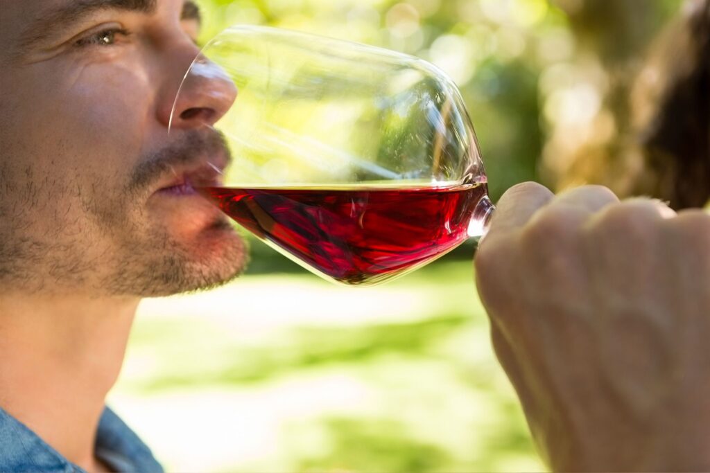 Ragazzo assaggia vino rosso con ambiente naturale sfocato nello sfondo.