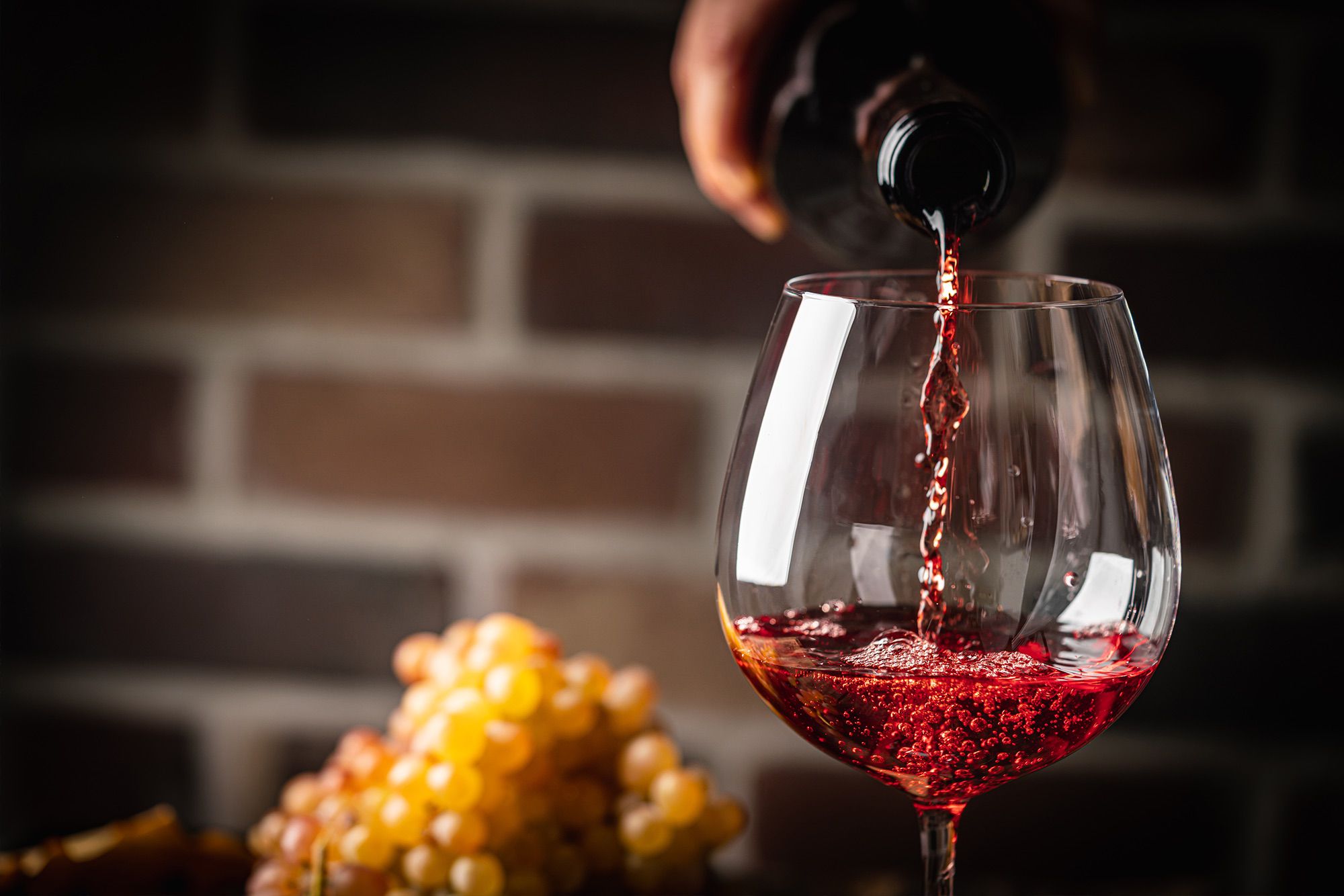Vino rosso versato in un calice con grappolo d’uva sullo sfondo.
