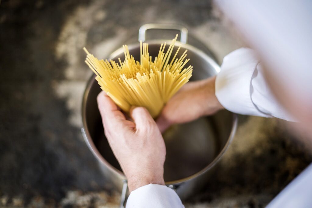 Chef a domicilio inizia a cuocere spaghetti in pentola.